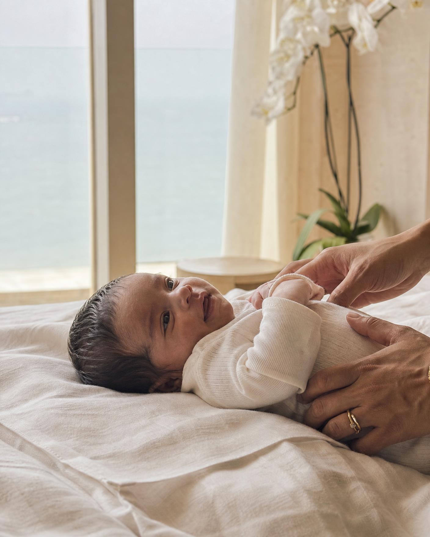 A newborn lying on a cream bed, watching a hanging mobile of stars and clouds